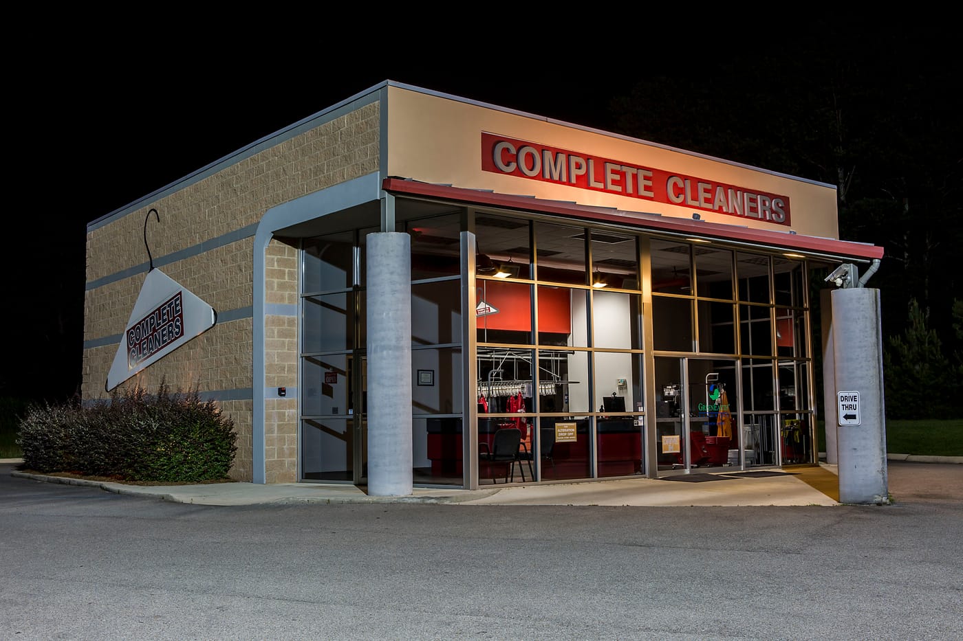 The Carrington storefront at night with the illuminated Complete Cleaners sign above the windows and the drive-thru lane to the right